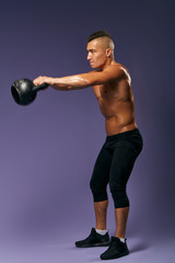 man performing swinging exercise with kettlebell, full length side view photo. isolated blue background, studio shot . sportsman holding weight with both arms, developing muscules