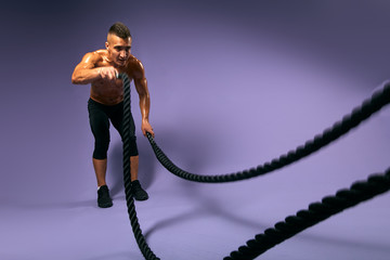 tired sportsman concentrated on doing exercises with ropes, guy preparing for a competition. full length photo. copy space.isolated blue background, fitness, crossfit