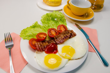 Breakfast with sunny side up fried egg, bacon, tomatoes, salad and tea