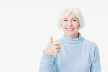 Senior lady showing thumb up gesture smiling on white background