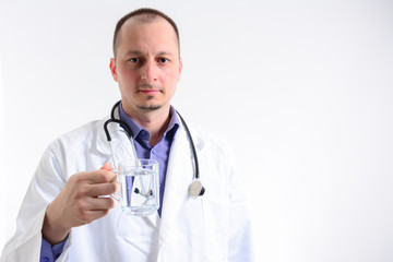 Fototapeta premium Portrait with copy space of cheerful joyful doctor in white lab coat and stethoscope on his neck, having a glass of water, looking at camera, isolated on grey background.