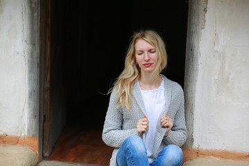 Fototapeta na wymiar Blond girl with mini jeans resting on the porch of an old Ukrainian-style house