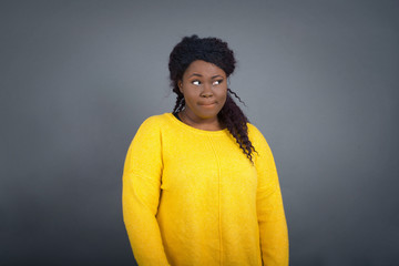 Photo of amazed puzzled young African American female with ginger hair knot, curves lips and has worried look, sees something awful in front, isolated on white background, dressed in jean overalls.