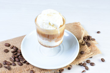 Cup of coffee with ice cream and coffee beans on white wooden background