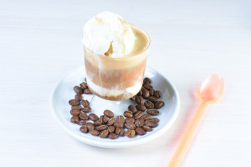 Cup of coffee with ice cream and coffee beans on white wooden background