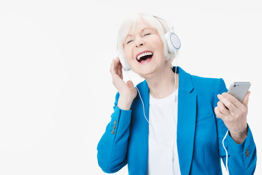 Senior woman with headphones listening music on phone and singing isolated on white background