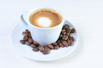 Maquiatto coffee cup with coffee beans on white wooden background