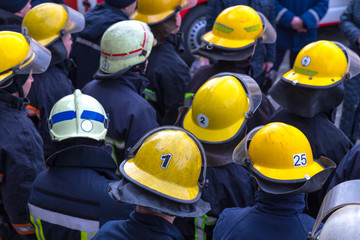 Fototapeta premium Firefighters in casks with personal numbers. Closeup on crowd of firefighters in yellow protective helmets.