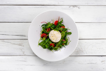 Fresh buratta with salad mix and juicy tomatoes on white wooden background.