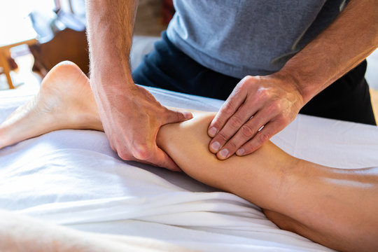 Young experienced masseuse doing therapeutic massage. Masseur working. Spa massage in a cosy home environment. Oil leg massage therapy
