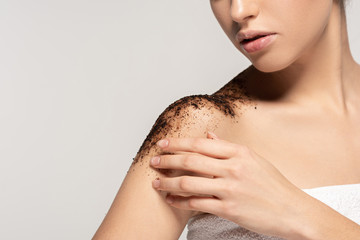 cropped view of girl applying coffee exfoliant on shoulders, isolated on grey