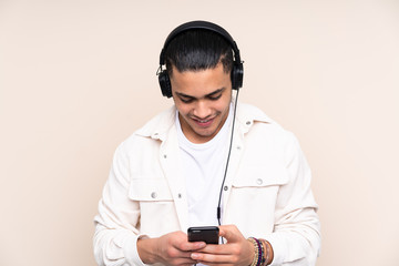 Asian handsome man isolated on beige background listening music and looking to mobile