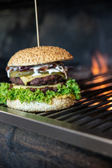 Duży burger ze świeżymi warzywami i serem owinięty w papier ekologiczny. Grillowana kanapka meksykańska na drewnianym stole w stylu industrialnym. Hamburger na wynos z widokiem na ogród. - obrazy, fototapety, plakaty