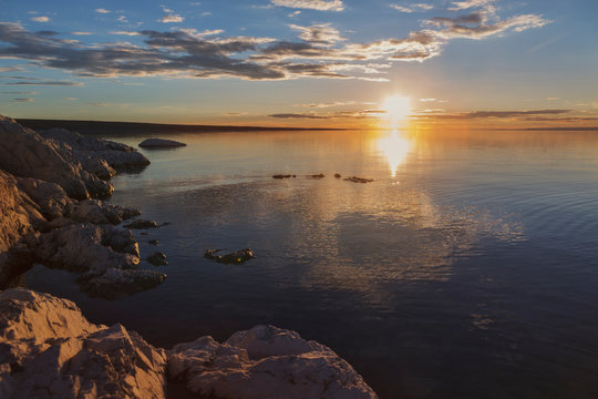 The setting sun with beautiful rays is reflected in the calm water of the lake. The shore of the lake with the remaining stones. Traveled photo in Mongolia.