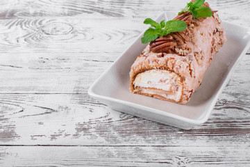 Meringue roulade with pecan nuts and cream cheese filling on the ceramic platter on the white wooden table
