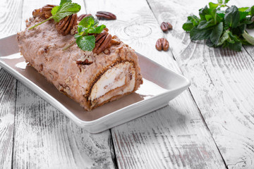 Meringue roulade with pecan nuts and cream cheese filling on the ceramic platter on the white wooden table