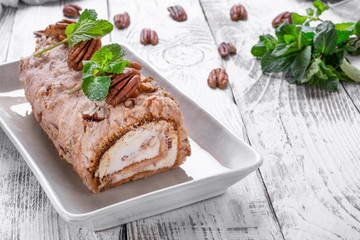 Meringue roulade with pecan nuts and cream cheese filling on the ceramic platter on the white wooden table