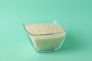 Glass square bowl with rice on mint background, space for text