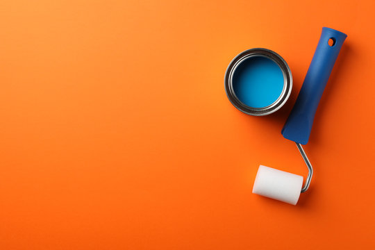 Can of blue paint and roller on orange background, top view