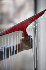 Window cleaner using a red squeegee to wash a window