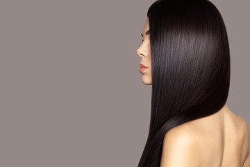 Hair care model. Hair cosmetics. Beauty fashion profile portrait of young brunette woman with smooth healthy long hair posing against gray background.