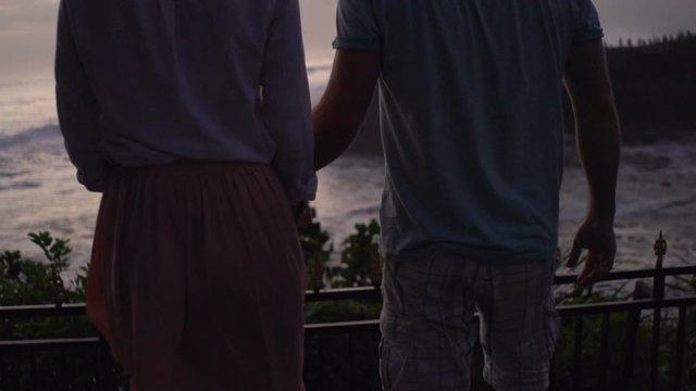 Young couple admire sunset above the beach, hold hands, slow motion