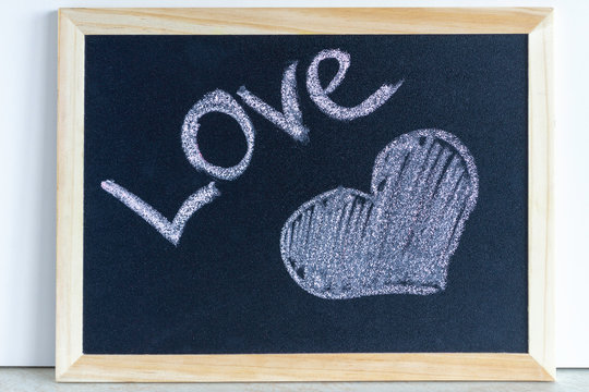 Heart painted with chalk and the inscription Love. Wooden chalkboard with picture. Valentine day and love concept.