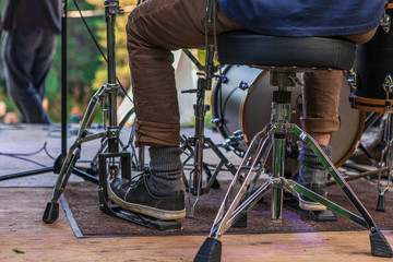 A closeup ground level perspective from behind a musician playing a drum set on a wooden stage...