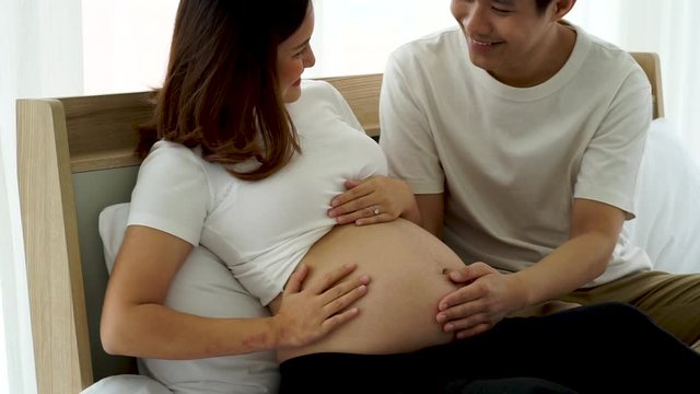 the Asian Young pregnancy woman  lay on the bed with her husband tenderness touch the bally with hands in the house 