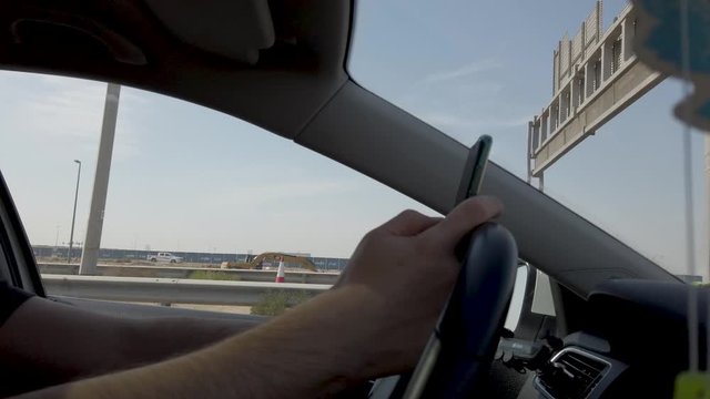 Male using his mobile phone to text or surf web while driving on the highway. Concept of unsafe driving. Using the phone wile driving is dangerous and can cause accidents.