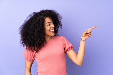 Young african american woman isolated on purple background pointing finger to the side and...