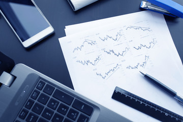 Top view of business chart on black table with with laptop, phone, pen, ruler and stapler