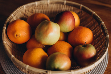  fresh fruits (apples and oranges) in a straw plate on a wooden table close-up