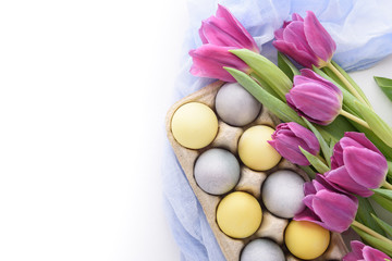 close-up of pastel blue and yellow Easter eggs with violet tulips with blue cloth napkin on white background