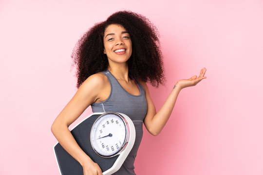 Young african american woman isolated on pink background with weighing machine