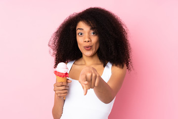 Young african american woman holding a cornet ice cream isolated on pink background surprised and...