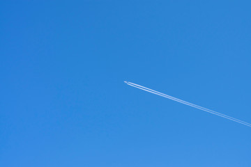 Bright blue sky background with white strip of airplane and free space for text. White plane flying high in the blue sky with a trace of the aircraft engines.