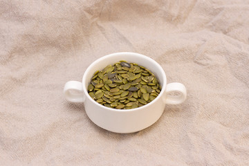 pumpkin seeds, in a white cup on natural linen. pumpkin seeds vitamins of group b and magnesium.