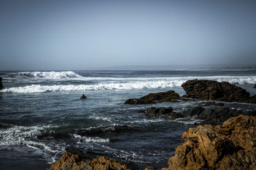 Playa con rocas caf&eacute;s y olas. bajo un cielo aul