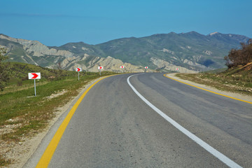 Winding country road in mountains . Asphalt road in the mountains with soft sky on the background. yellow and white line . Mountain road in poor condition .