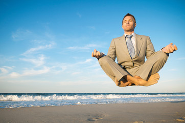 Levitating businessman closing his eyes with crossed legs above a tranquil beach scene