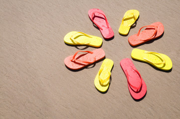 Sunny circle of flip-flops in bright colors sitting on smooth sand beach