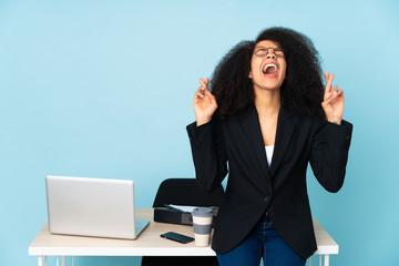African american business woman working in her workplace with fingers crossing