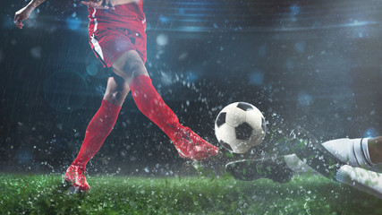 Football scene at night match with player in a red uniform kicking the ball and opponent in tackle to defend