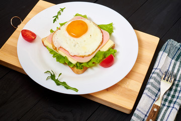 Toast with ham, egg and tomato on a plate on a black background.