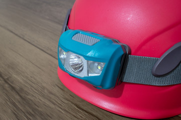 Teal led headlamp turned off strapped to a pink climbing helmet on a wooden table © Everton