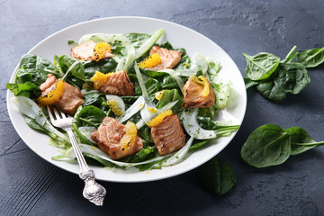 Leafy salad with red fried fish and orange on a white plate with a fork on a grey background. Background image, copy space