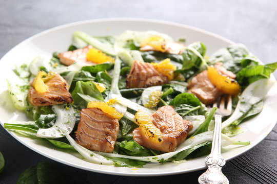 Leafy salad with red fried fish and orange on a white plate with a fork on a grey background. Background image, copy space