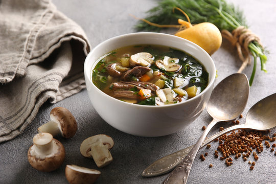 Concept of Russian cuisine. Soup with mushrooms and turnips. Near greens, spoons and buckwheat on a light background. Background image, copy space