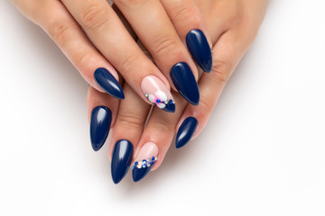 Dark blue manicure on sharp long nails with orchids and white, blue crystals on the ringless...